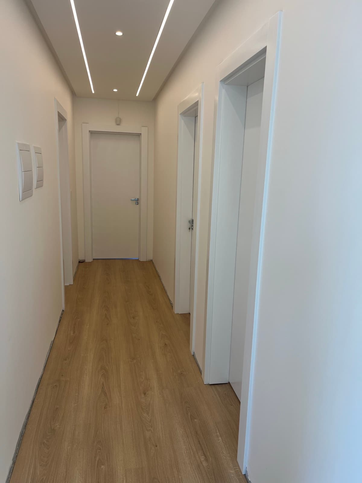 Corredor com portas brancas, piso amadeirado e rodapé branco instalados
