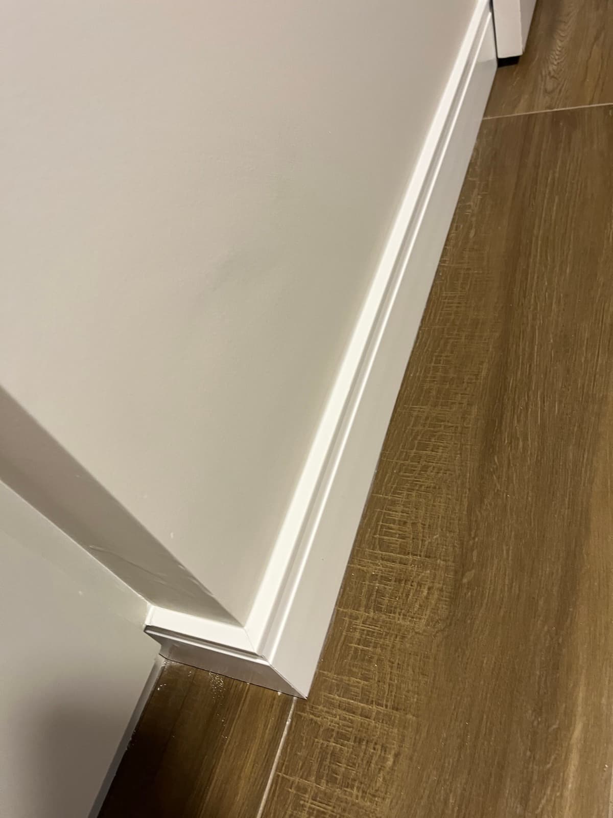 Detalhe de rodapé branco junto ao piso amadeirado e à guarnição da porta
