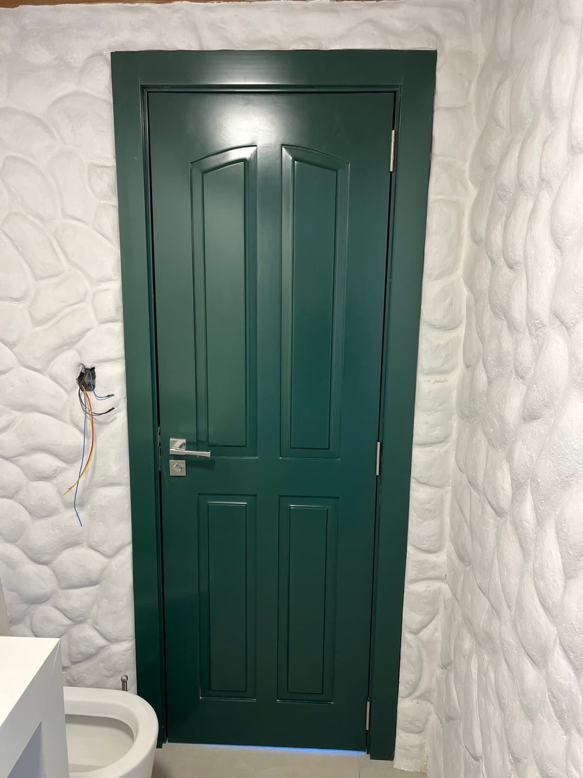 Porta verde de quatro painéis junto a parede de pedra